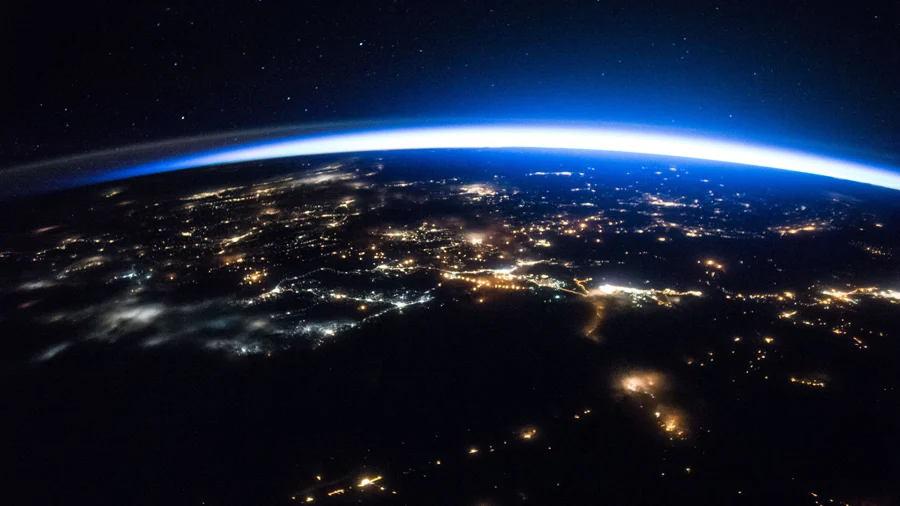 The curved horizon of Earth glows blue above city lights at night, viewed from orbit.